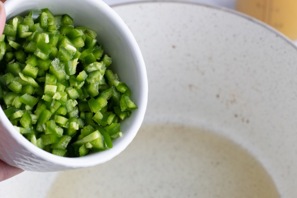 Pouring diced jalapenos into pan