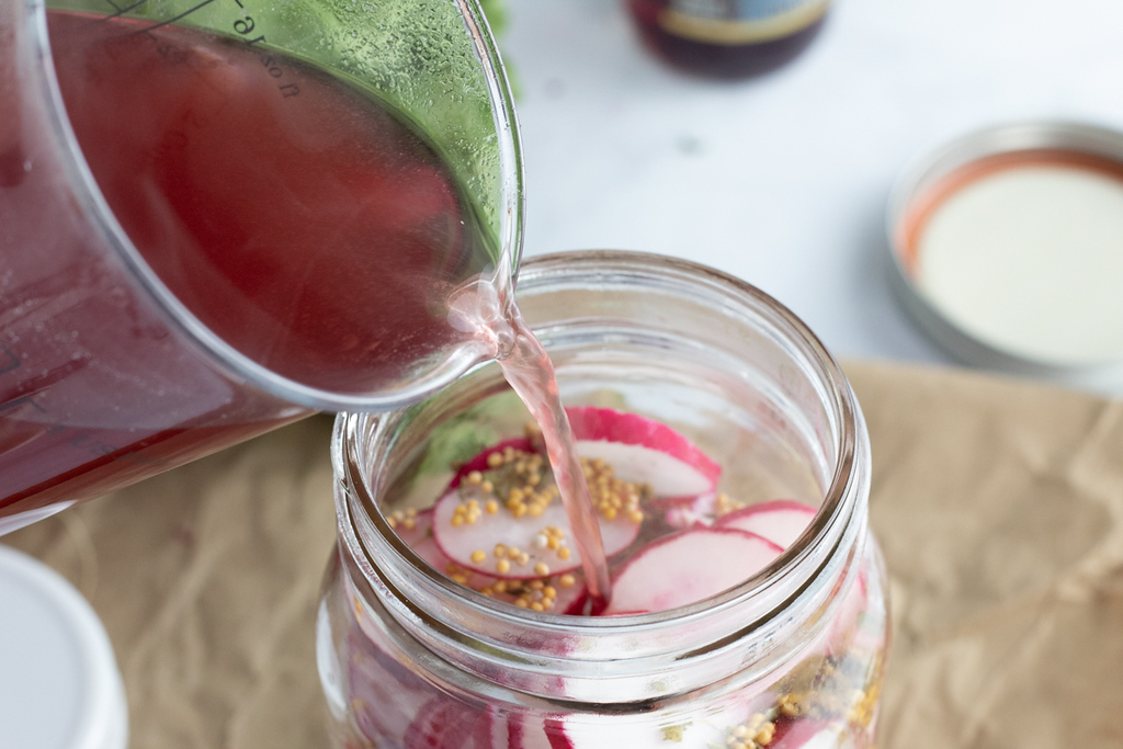 pouring brine into jar of radishes 
