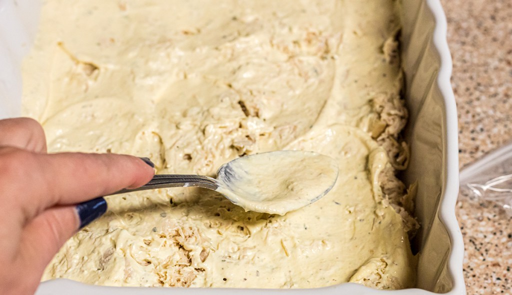 using spoon to spread out sauce on keto chicken cordon bleu casserole