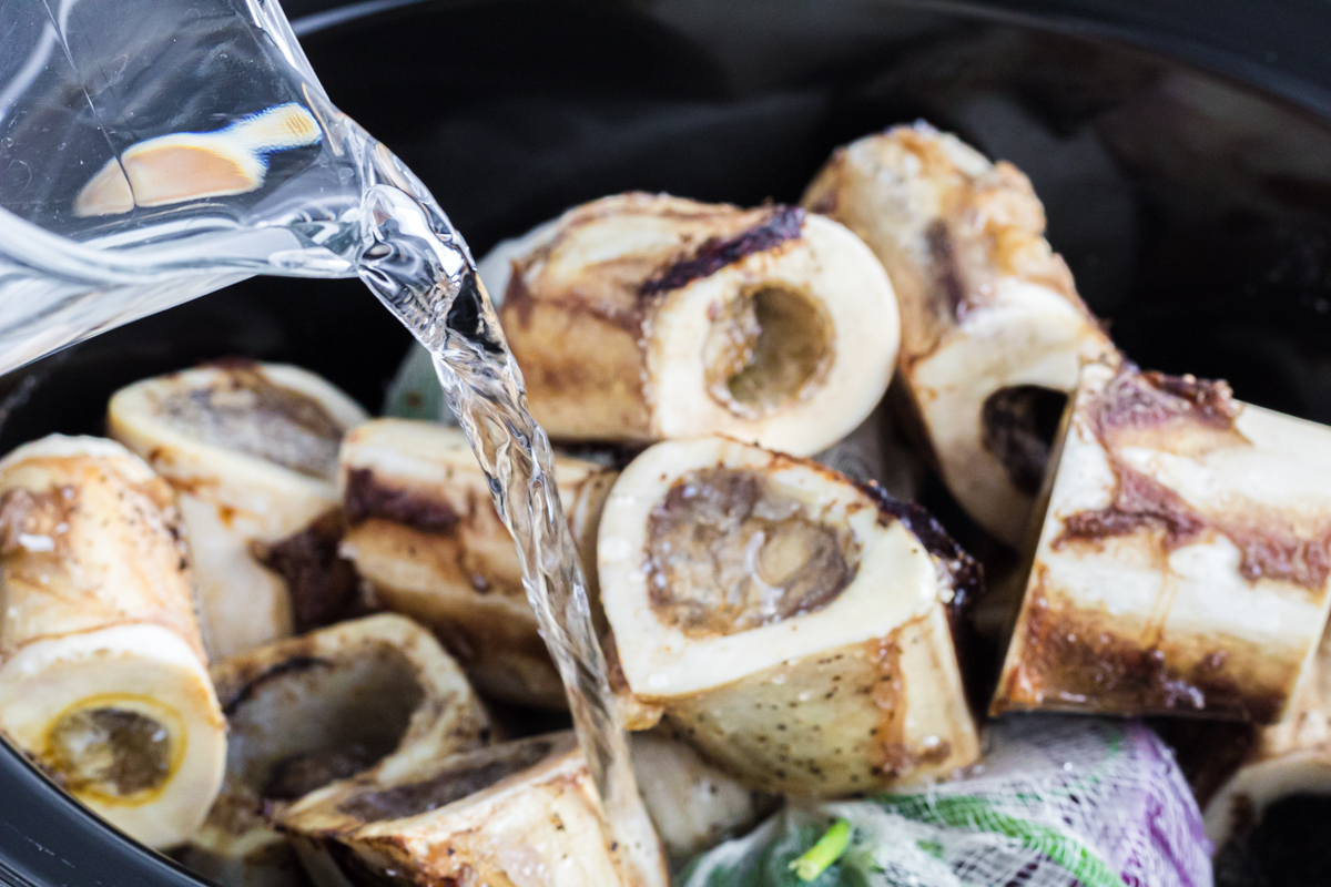 pouring water over bones and vegetables in slow cooker