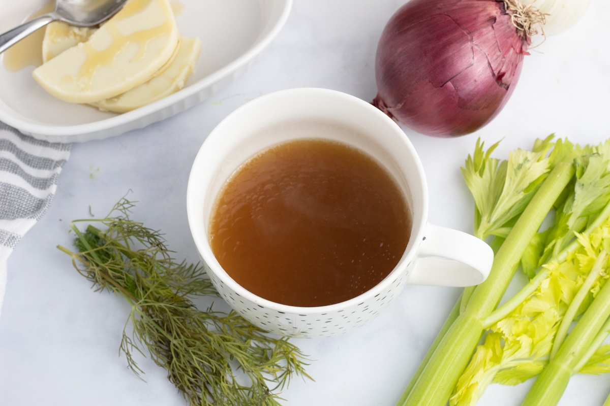 mug filled with homemade bone broth with celery and onion next to the cup