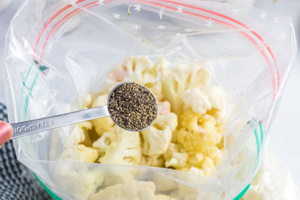 pouring pepper into bag of cauliflower florets