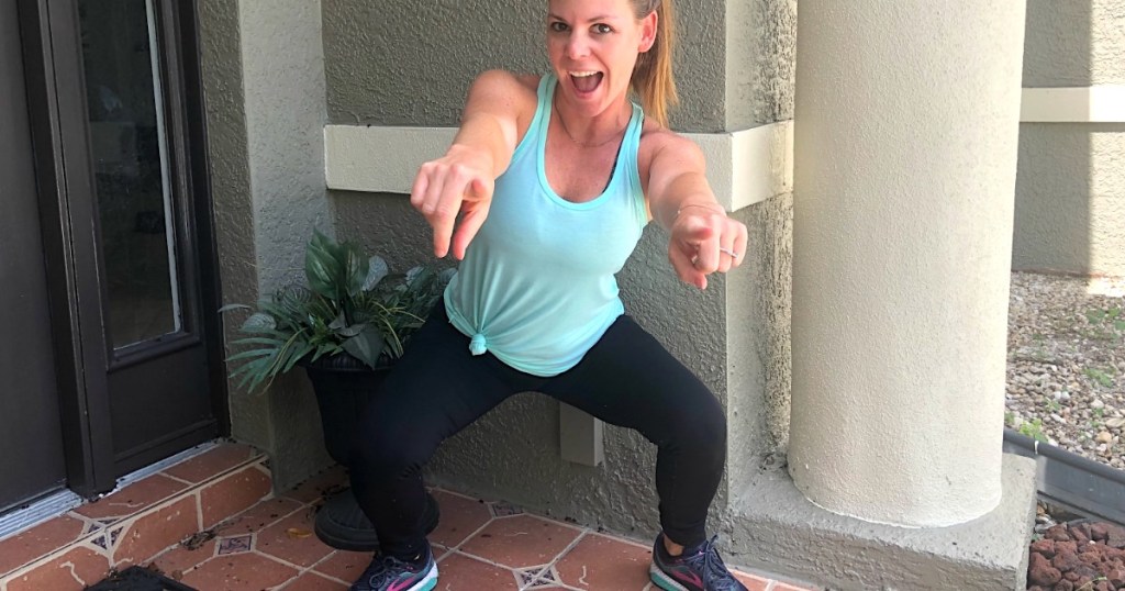 woman doing squats and pointing at camera 