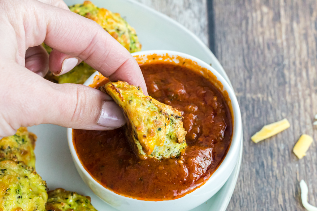 dunking zucchini bites into marinara sauce 