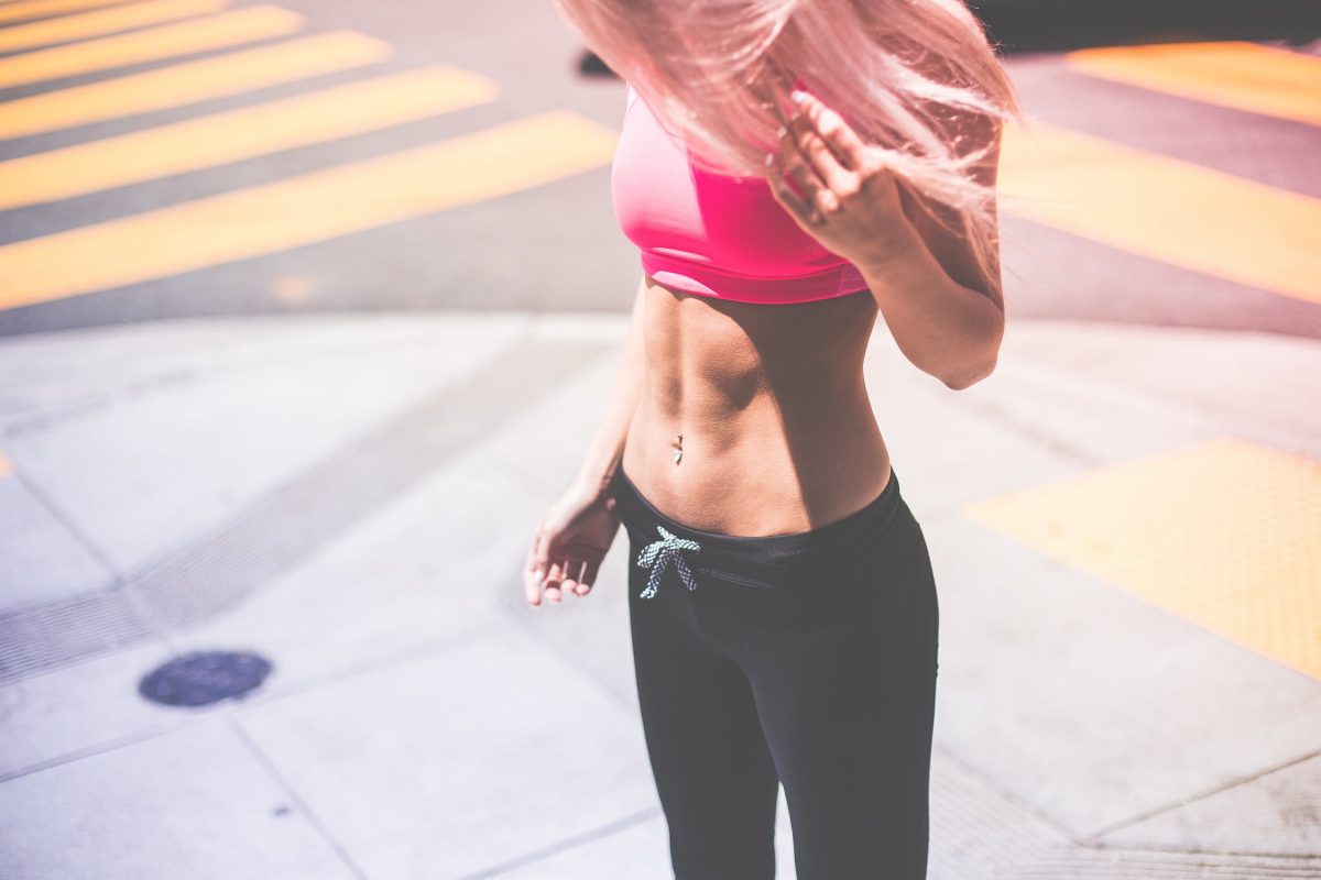 woman wearing pink sports bra looking at stomach 
