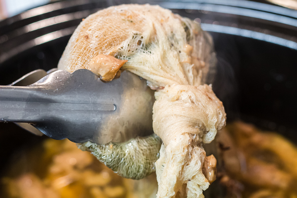 taking cheesecloth filled with herbs and veggies out of bone broth