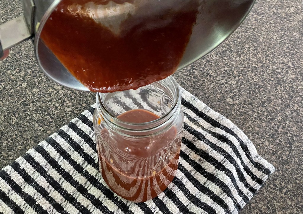 pouring keto bbq sauce into a jar 