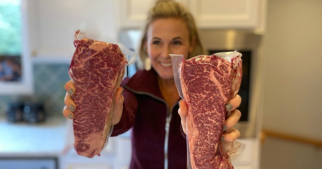 woman holding well marbled ribeye steaks