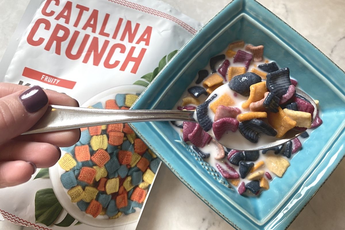 A hand grabbing a spoon out of a bowl of cereal next to the cereal bag on a counter