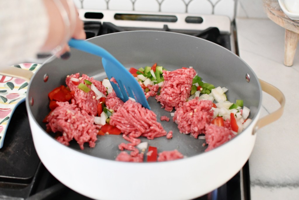Crumbled ground beef in a skillet with onion and bell peppers.