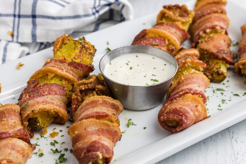 bacon wrapped pickles on a plate with a side of ranch dressing