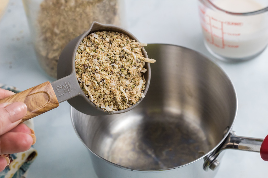 pouring 1/2 cup keto oatmeal in saucepan 