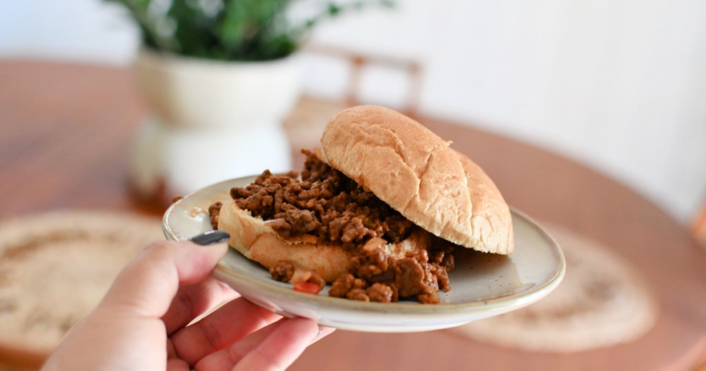 a woman is holding a plate with a keto sloppy joe sandwich.