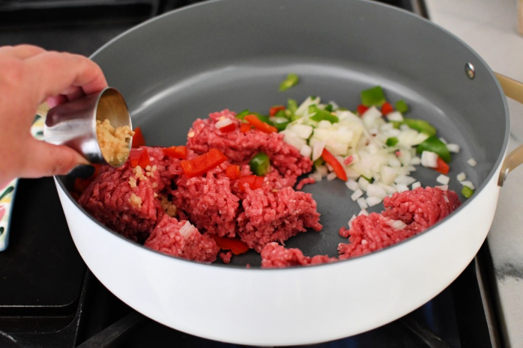 Adding chopped garlic to keto sloppy joes in a skillet.