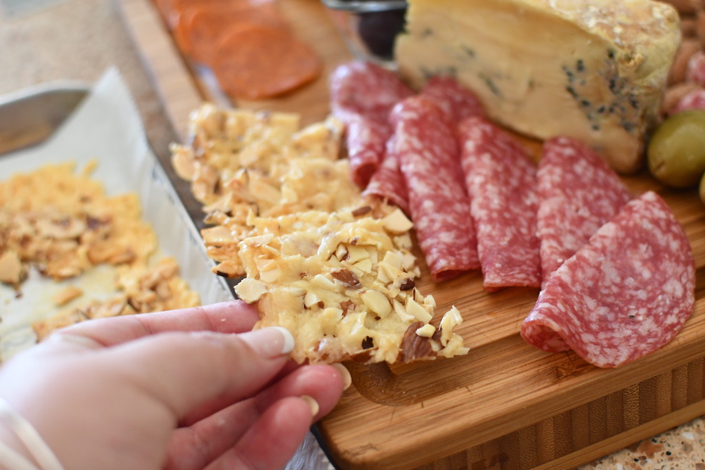 holding keto cracker near salami and cheese on tray 