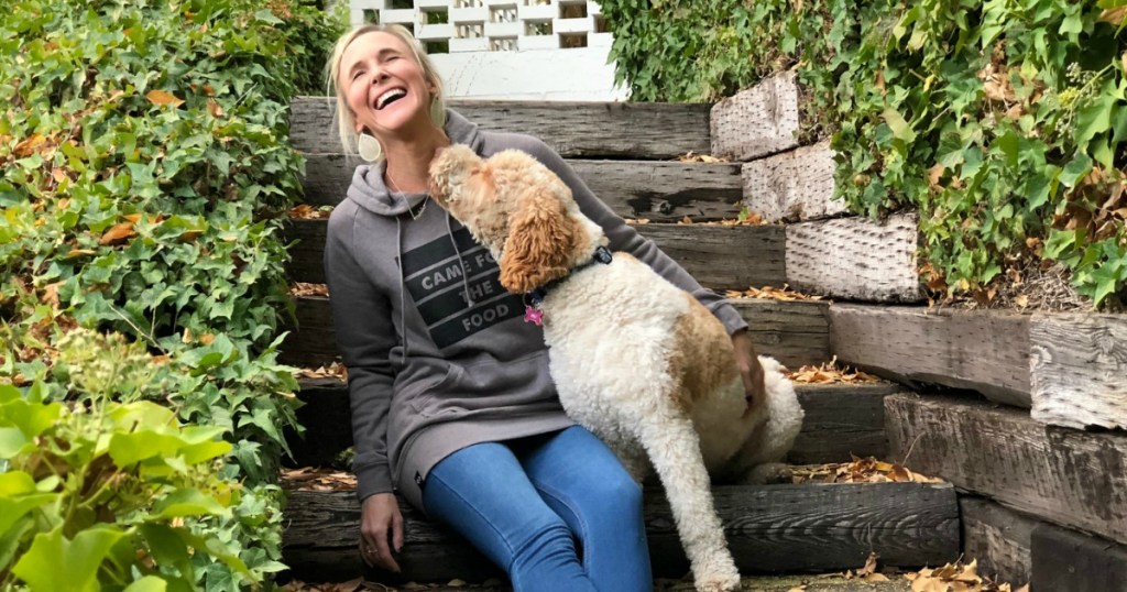 woman laughing on front porch as dog is licking her