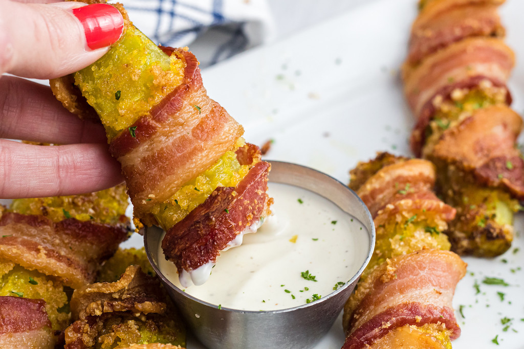 dipping bacon-wrapped pickle in ranch dressing 