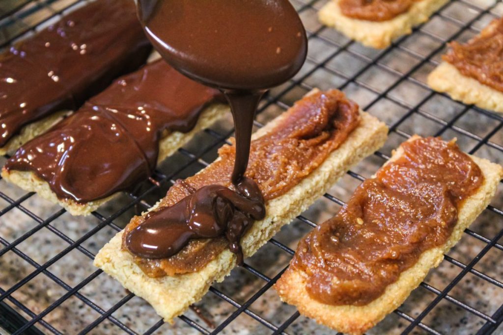 pouring melted chocolate over shortbread cookie bars