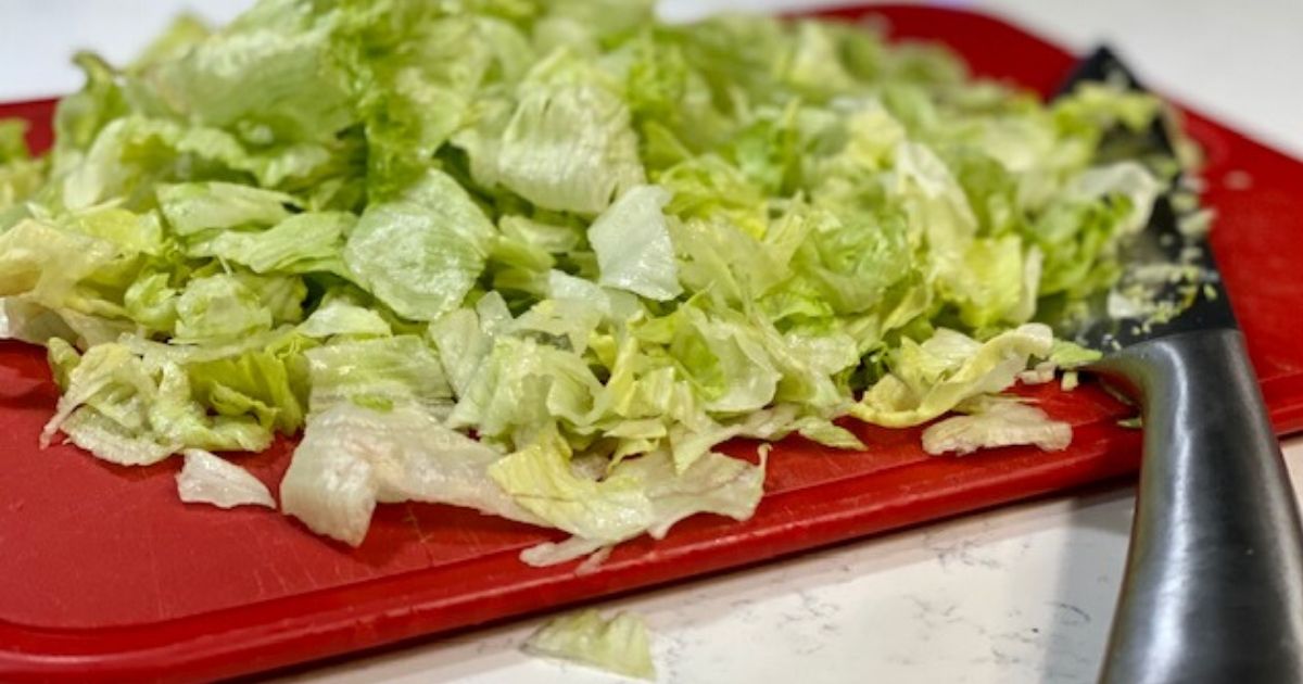 Chopped Iceburg lettuce, one of our favorite low carb veggies, on a cutting board with knife