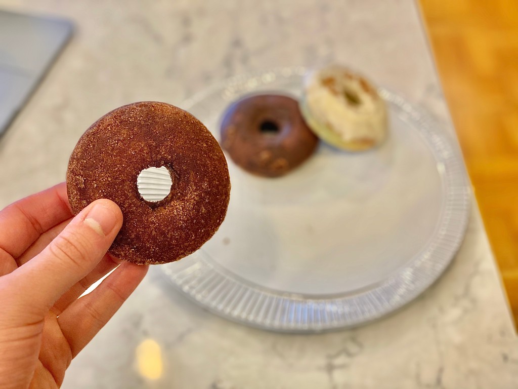 holding low-carb cinnamon donut with two donuts in the background on a plate