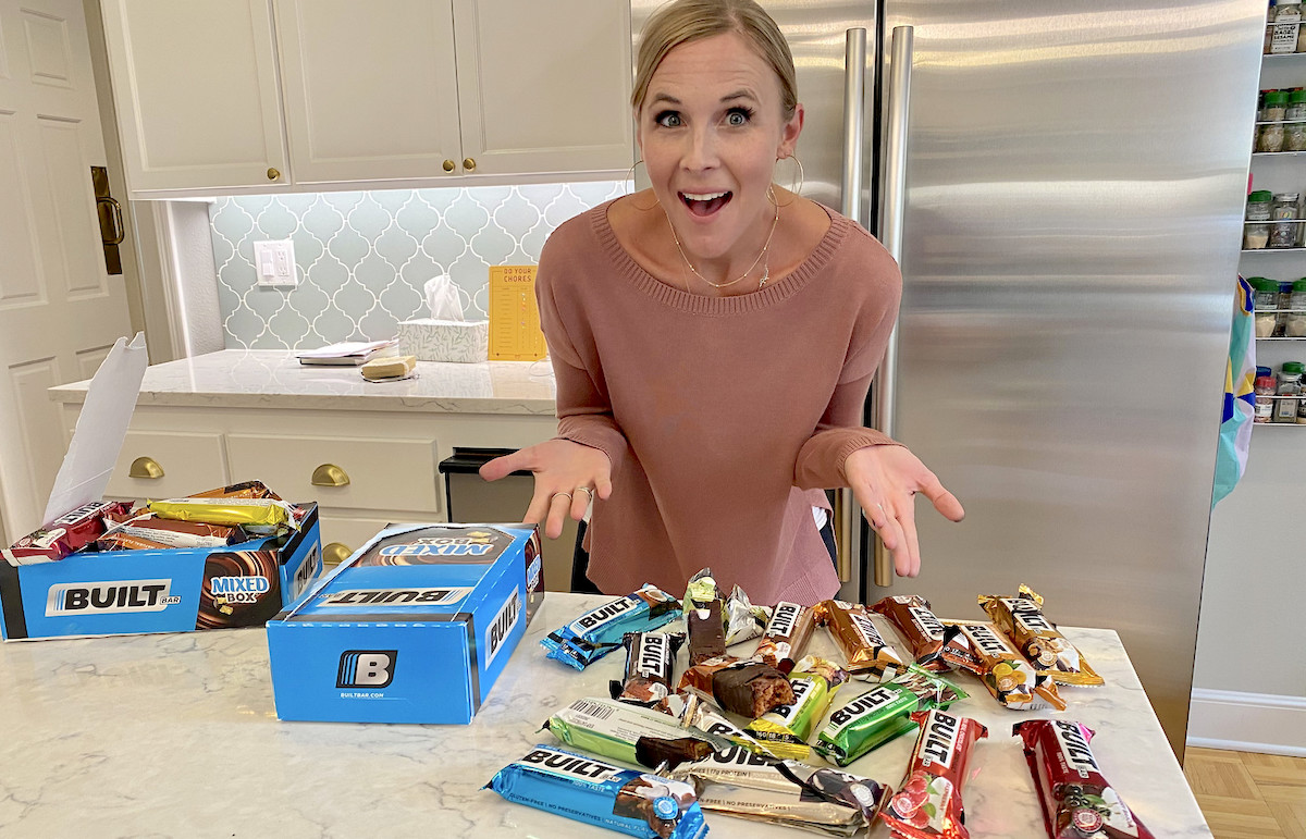 woman standing in kitchen with arms out over countertop full of built bars keto bar