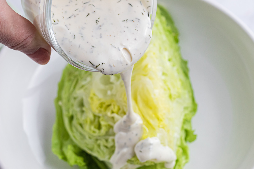 pouring ranch dressing on iceberg lettuce 