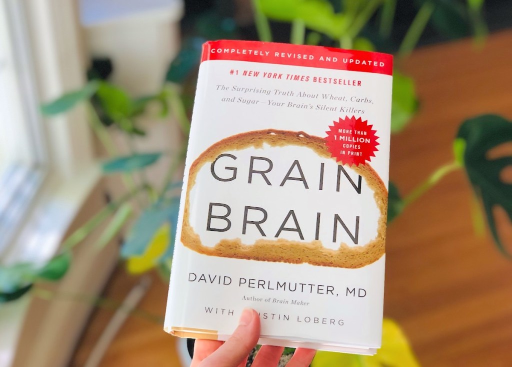 hand holding a Grain Brain book in front of plant