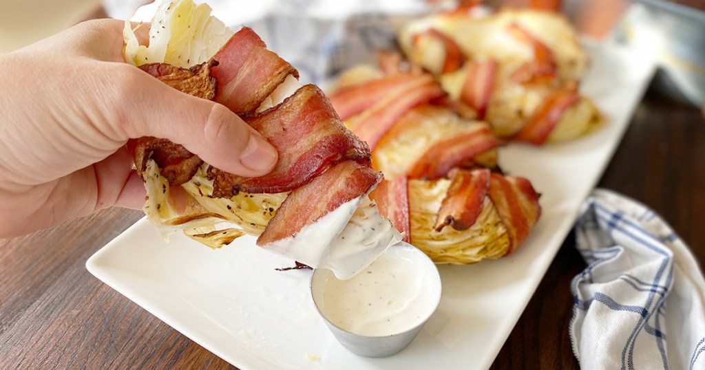 hand holding bacon wrapped cabbage wedge and dipping it in ranch