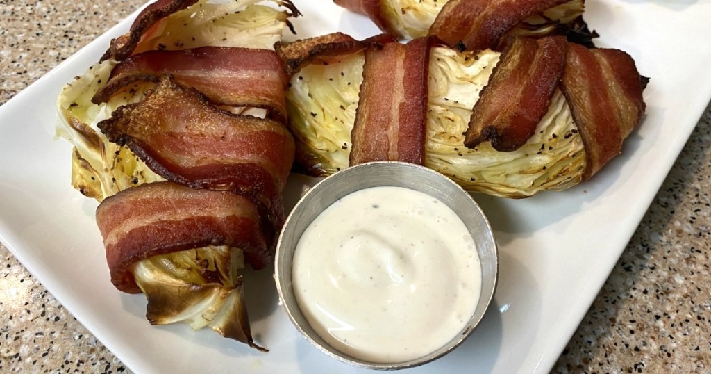 bacon wrapped cabbage wedges on plate with ranch dressing