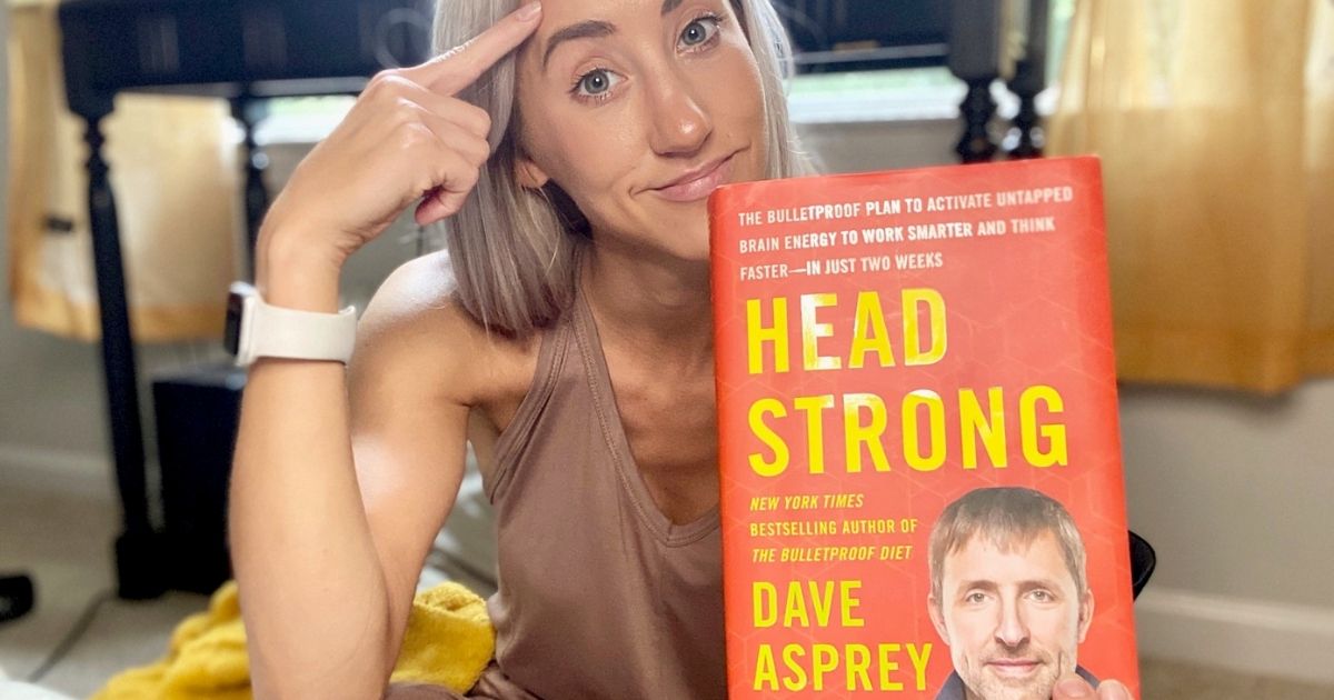 Woman holding a hard copy of Head Strong and pointing to her head