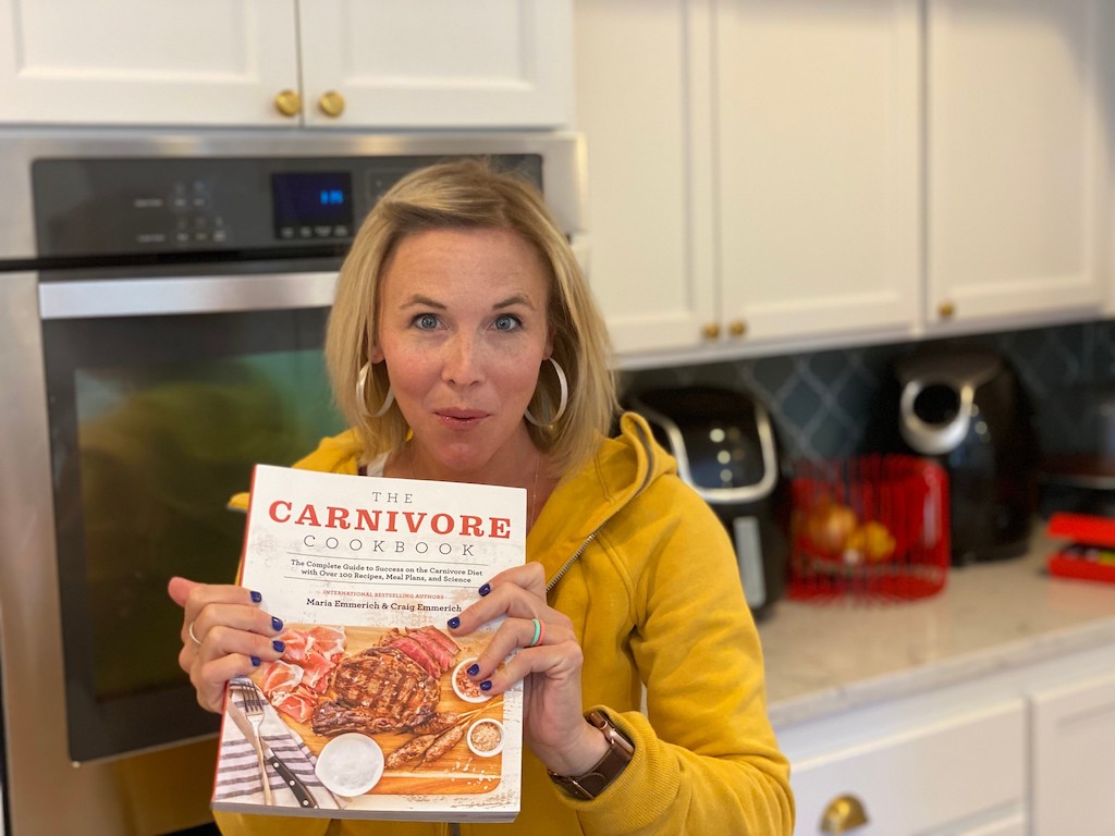 woman holding The Carnivore Cookbook in the kitchen