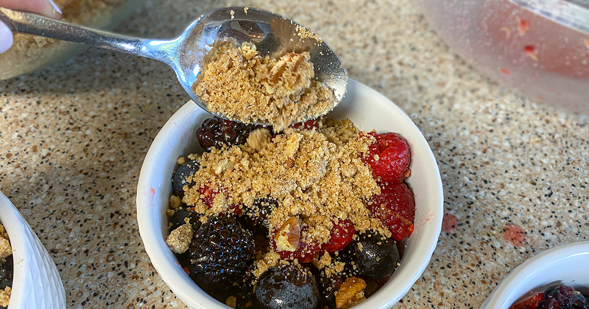 pouring crumble topping on berry cobbler