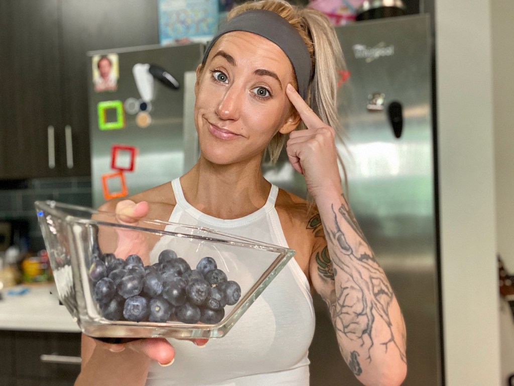 woman holding clear dish of blueberries