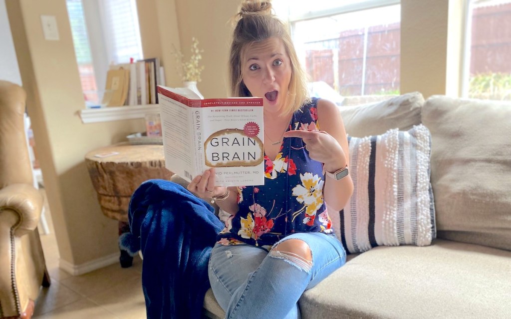 Woman sitting on couch pointing to grain brain book