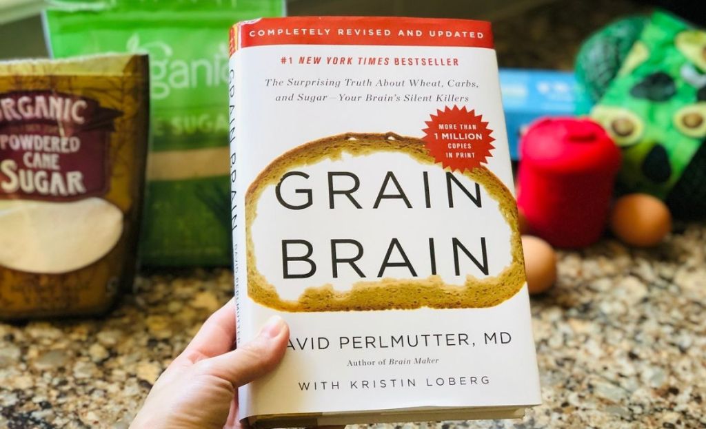 A hand holding a copy of Grain Brain in front of sugar