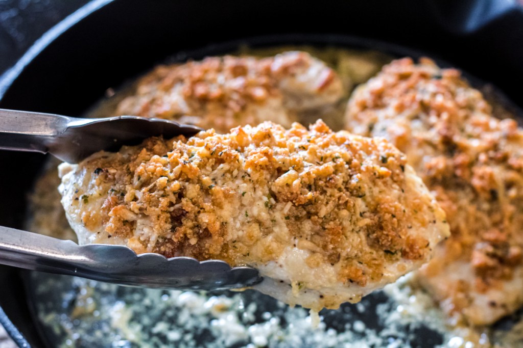 taking out a piece of chicken from a cast iron skillet