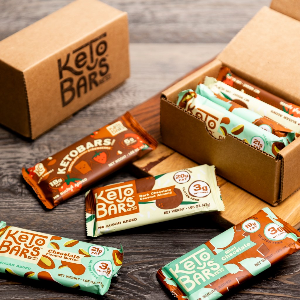 A sample box of keto bars next to some bars on a table