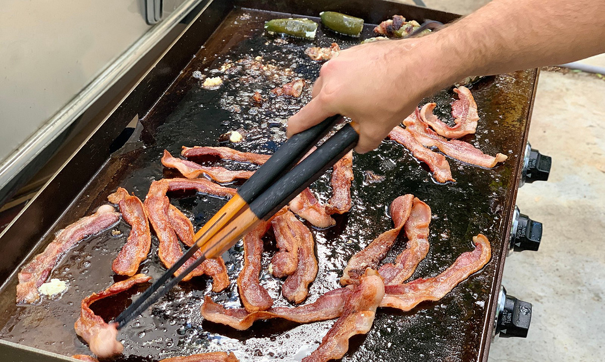 man using tongs to pick up bacon on Blackstone griddle