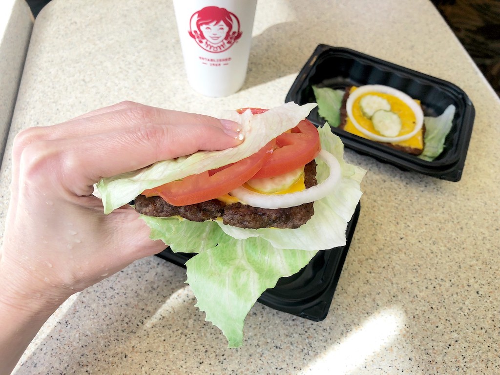 holding Wendy's bunless keto burger wrapped in lettuce 
