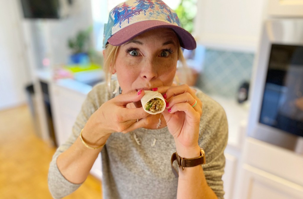 woman eating jicama wraps wearing hat