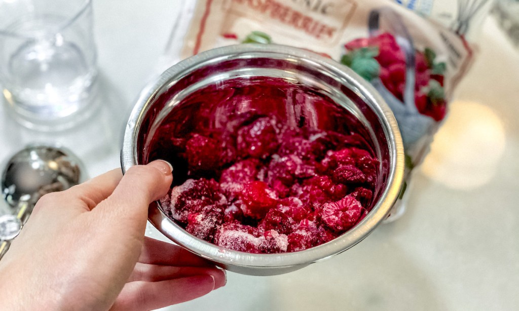 hand holding a stainless steel bowl with frozen raspberries inside
