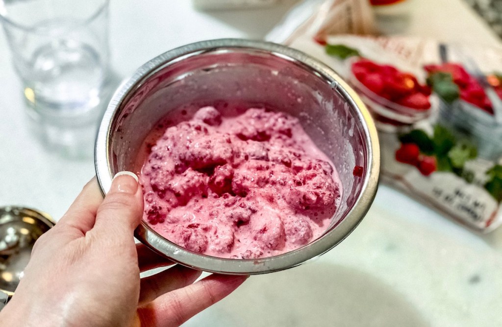 hand holding a stainless steel bowl with pink raspberry smoothie inside