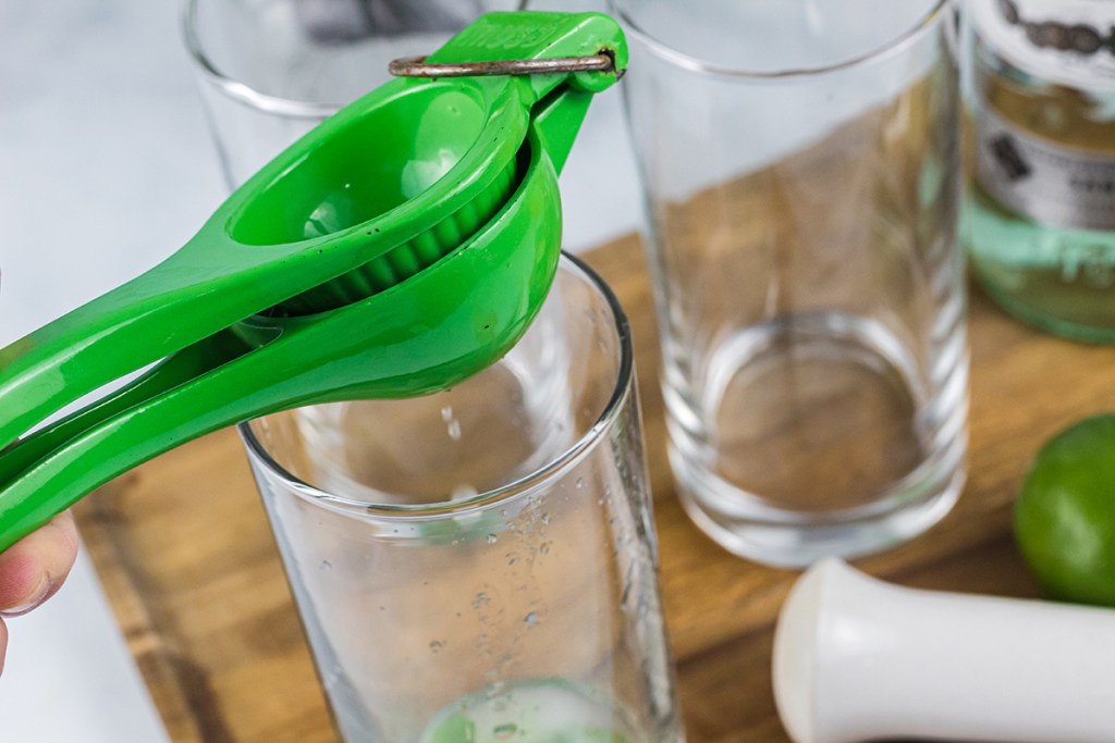 using a citrus juice to squeeze lime juice into glass