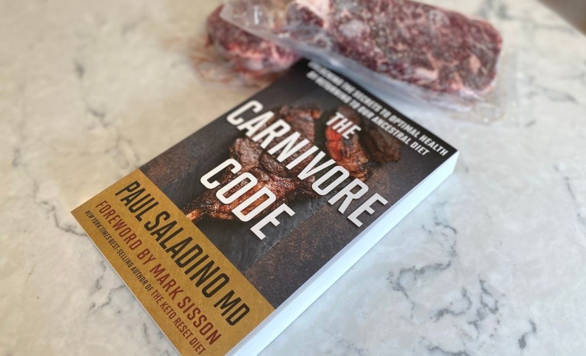 The Carnivore Code book on a counter next to some steaks