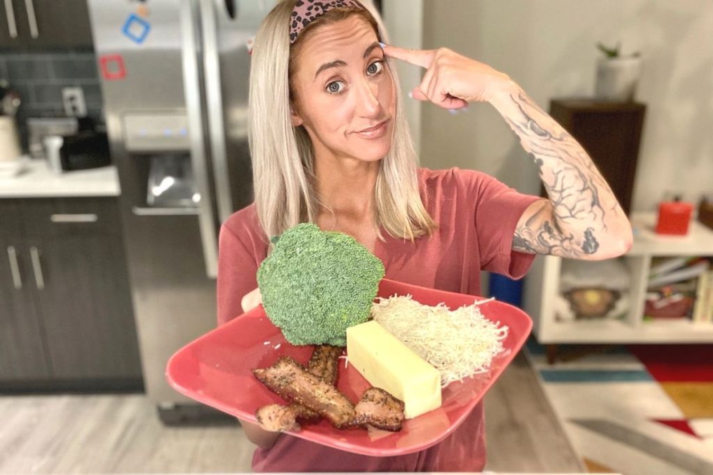 A woman holding a plate with cheese, bacon, butter, and broccoli on it