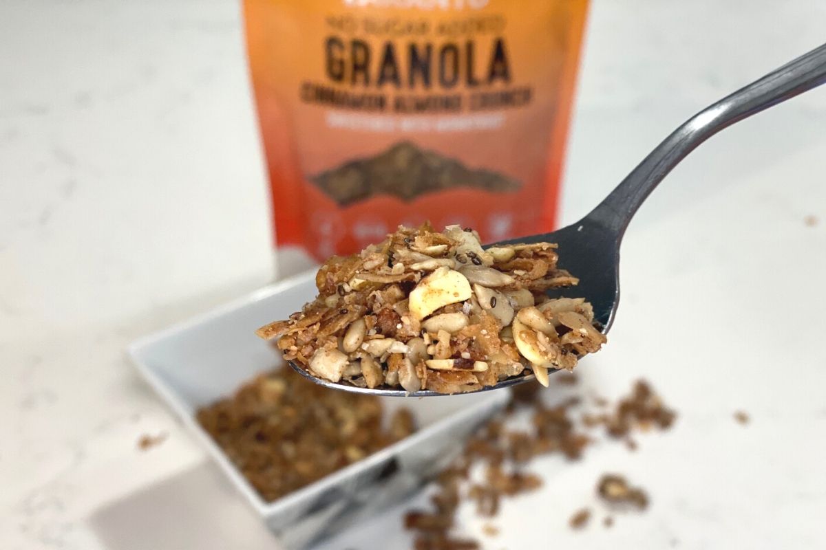 A spoonful of granola in front of a bowl and bag of granola