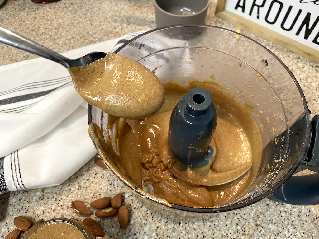 taking spoonful of homemade almond butter out of food processor