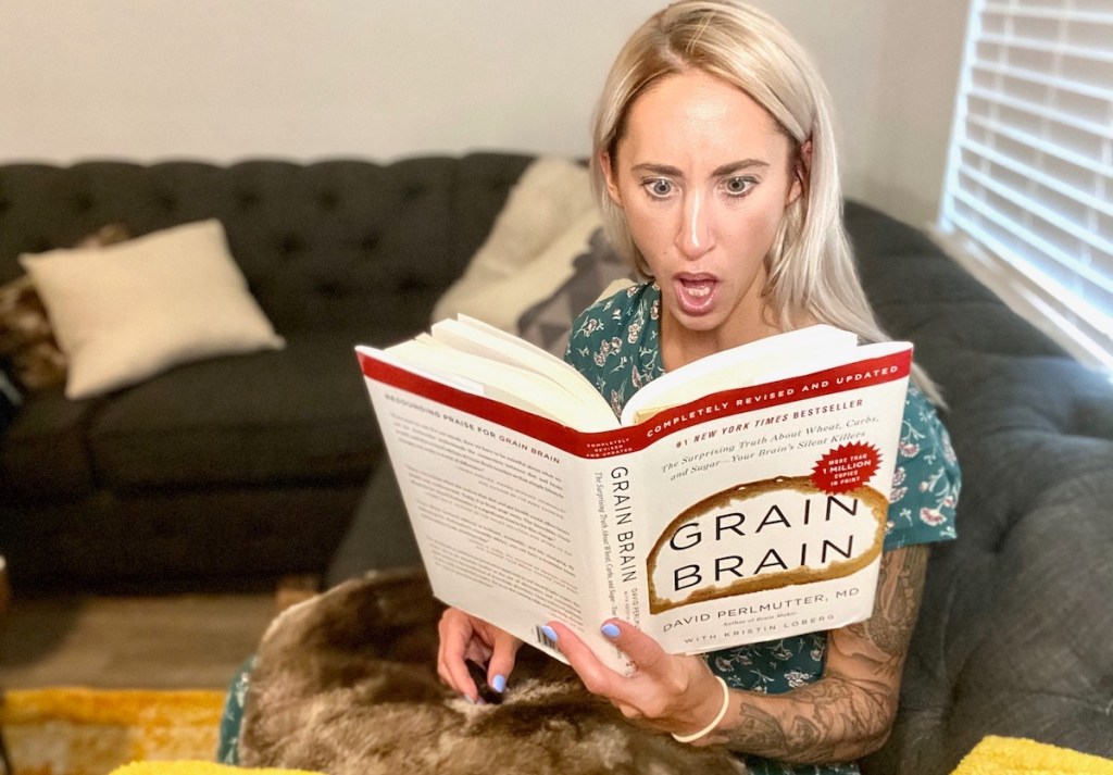 woman holding grain brain book looking shocked sitting on couch