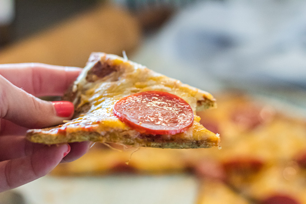 holding slice of pork rind pepperoni pizza 