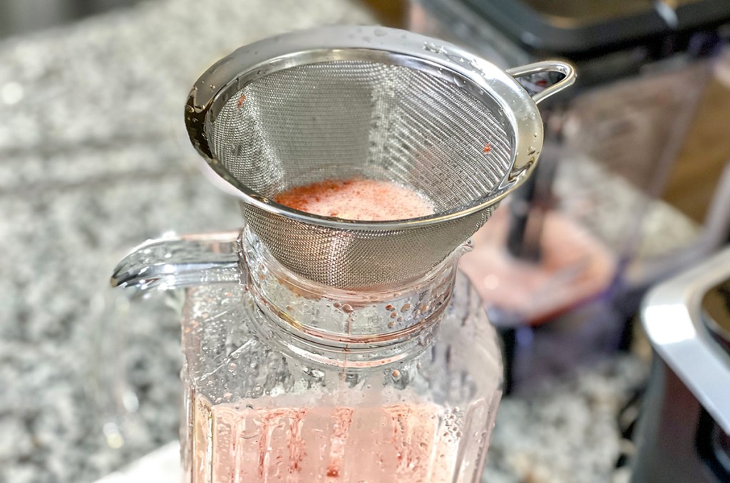 straining strawberry pulp into pitcher